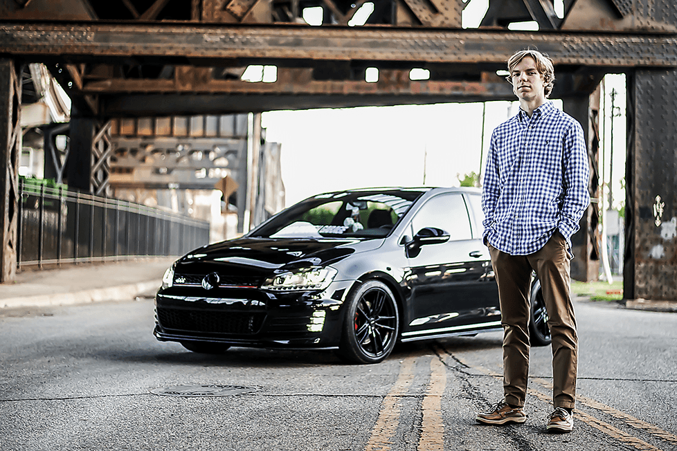 A boy standing by his black Volkswagen Golf under a train trellis in Cincinnati.