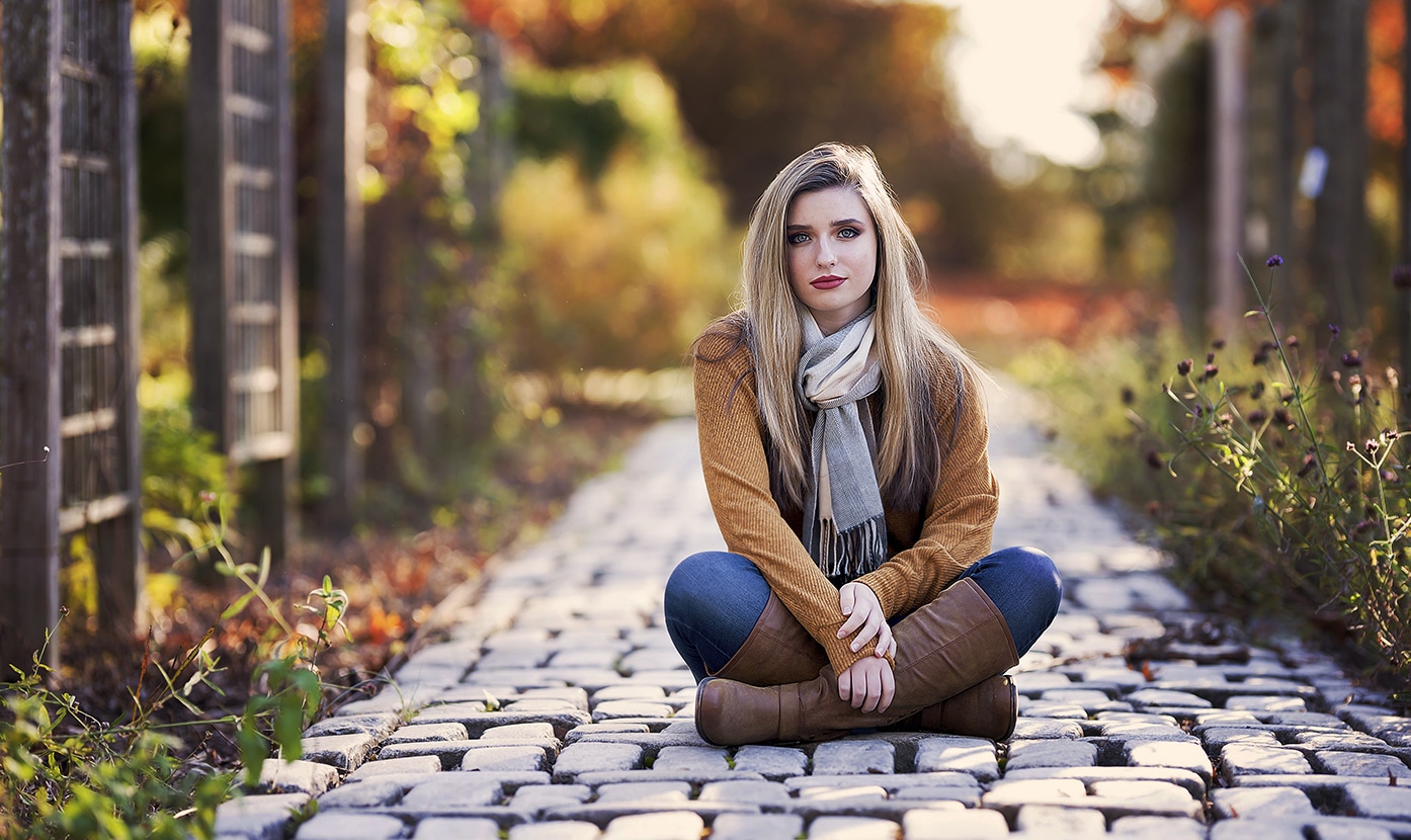 High school senior girl dressed in fall clothes sitting on a cobblestone path in Mt Airy Forest in Cincinnati