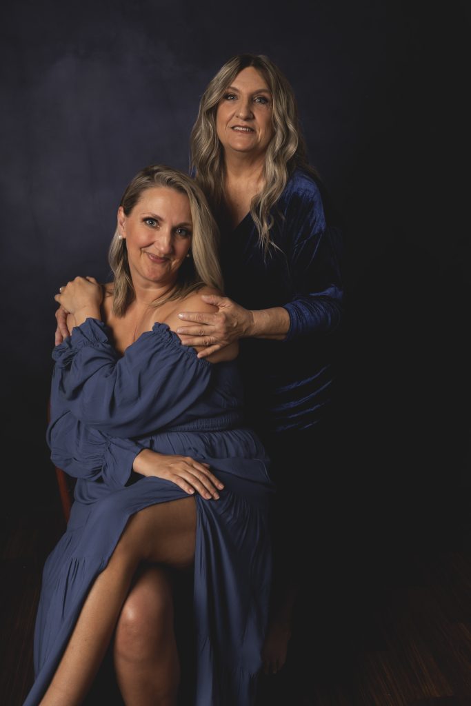 fine art portrait of a mother and adult daughter in blue dresses on a blue background with studio lighting by tonya bolton photography