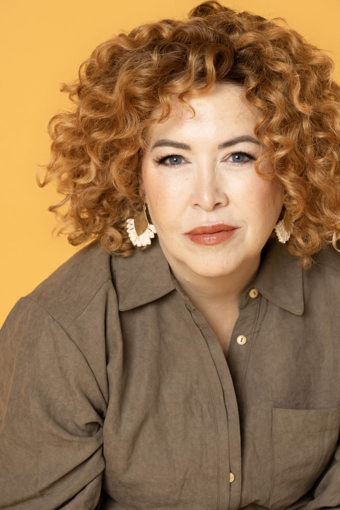 A professional headshot by tonya bolton photography of a woman in the beauty industry. She is a redhead on a yellow portrait backdrop.