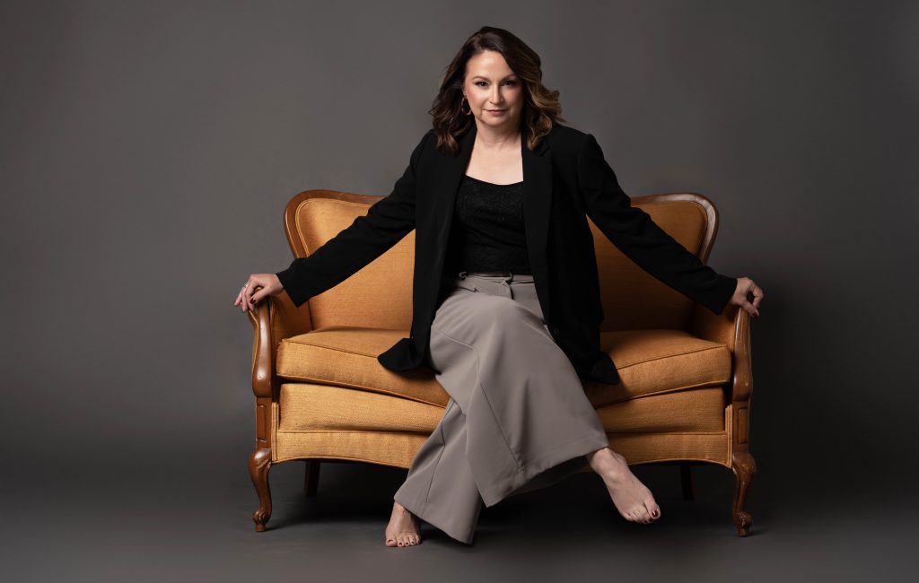 A portrait of an empowered woman in a bold pose on a gold sofa, who looks like she is ready to take on the world. Taken by Tonya Bolton Photography.