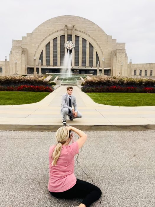 Behind the scenes image showing photographer, Tonya Bolton, photographing a high school senior boy in a suit in front of Union Terminal in Cincinnati Ohio
