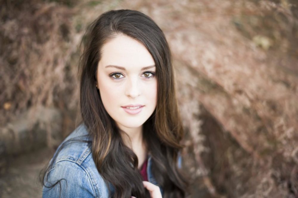 High school student sitting in front of spring foliage for her senior pictures in Eden Park