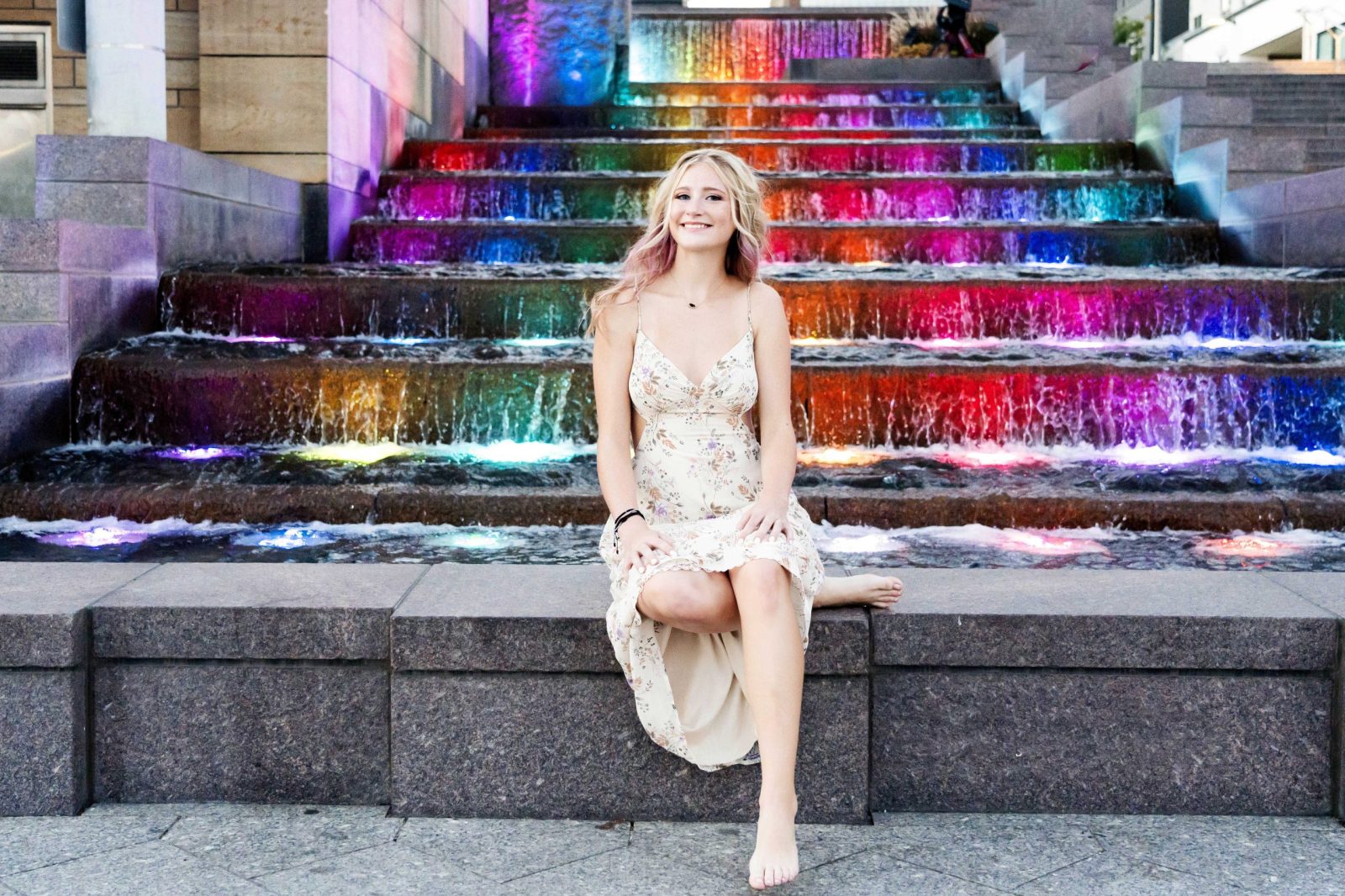 High school senior in a floral dress sitting casually on the base of the fountain at smale park in cincinnati