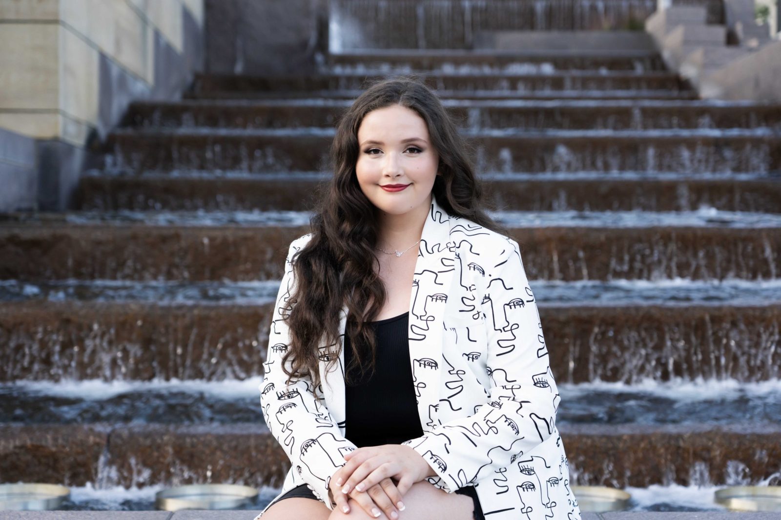 a senior photo of a girl in a white patterned blazer sitting on the fountain at smale park in cincinnati with tonya bolton photography