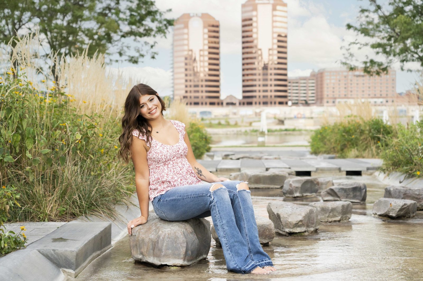 a high school senior girl sitting on a rock in a water fountain for senior pictures at smale park in cincinnati with tonya bolton photography